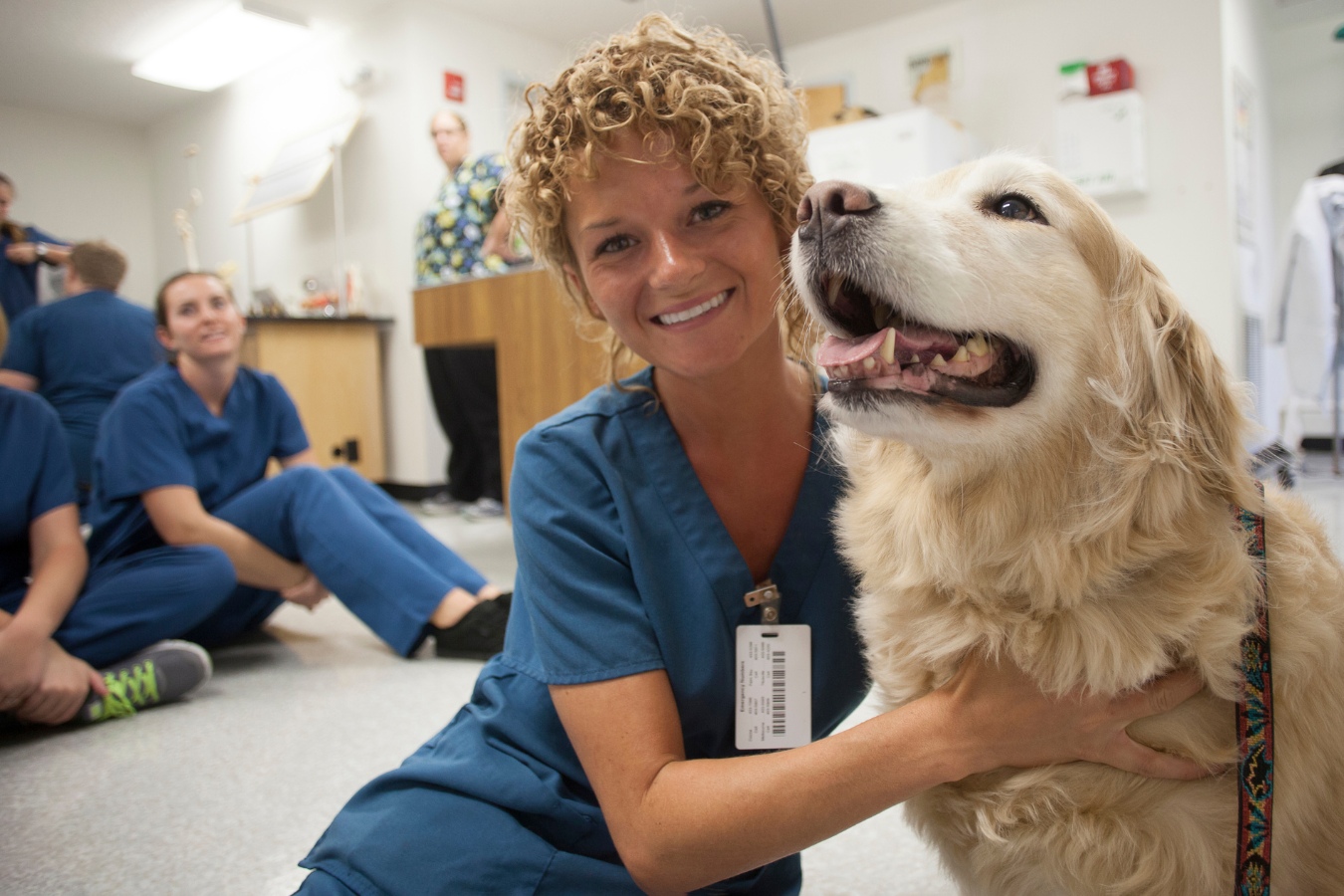 Joyful female veterinary nursing student smiling while interacting with a dog in the classroom.