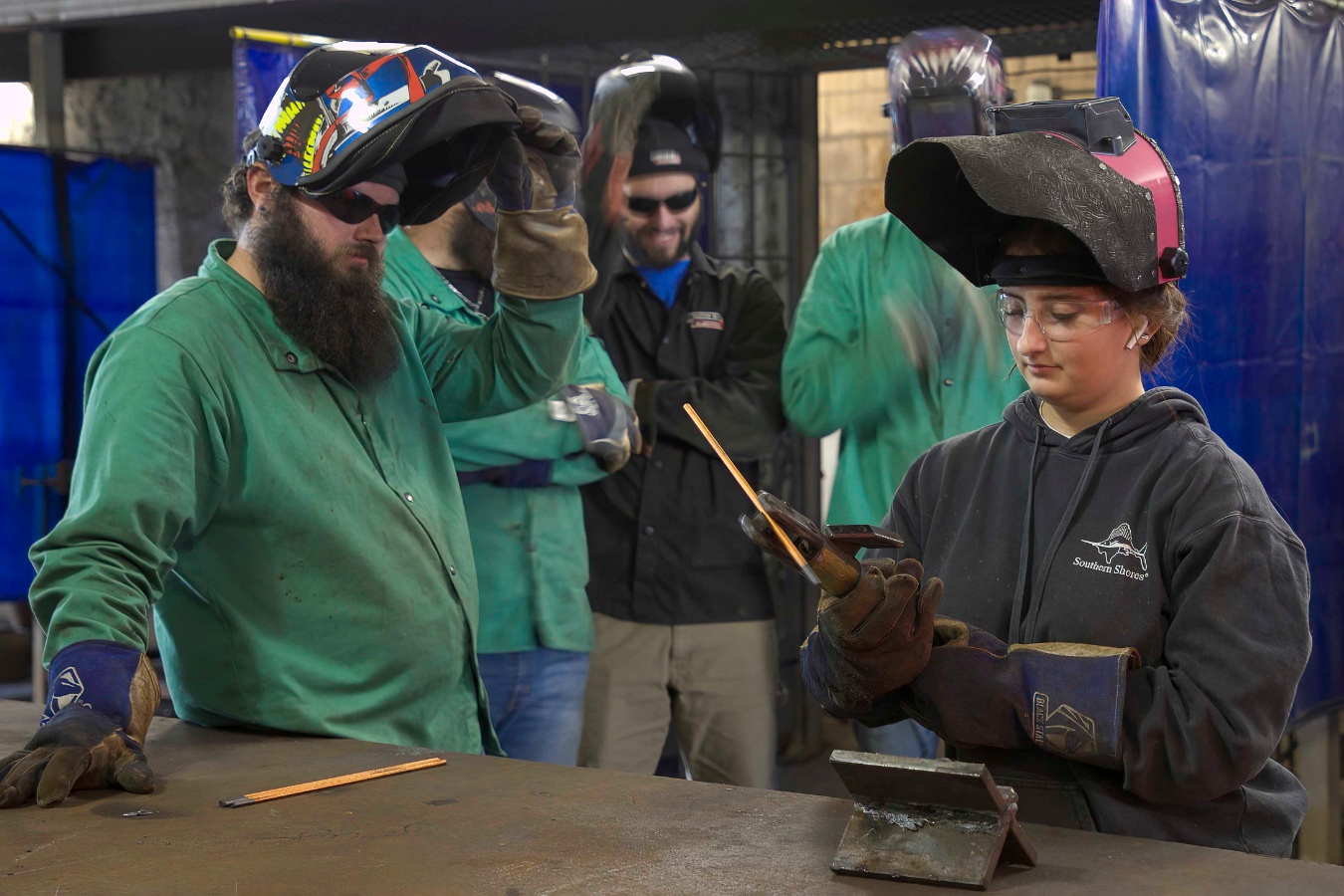 Group of welding students, with a female student in focus, working on a project.