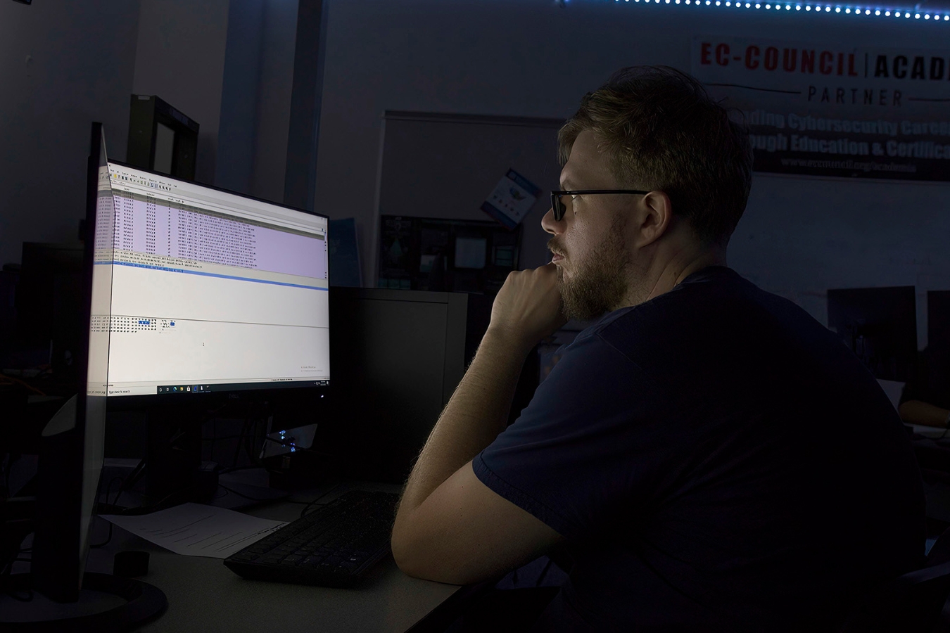 Focused student working on a coding project for a cybersecurity class in a dimly lit classroom, encouraging maximum focus.