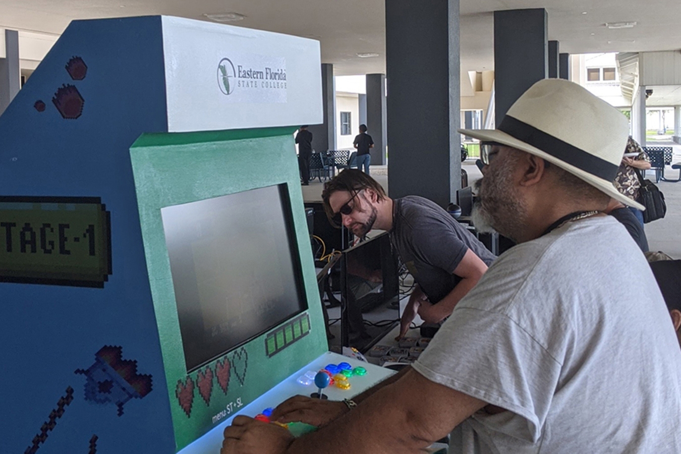 Male student with a hat playing an arcade-style game at a student club event.