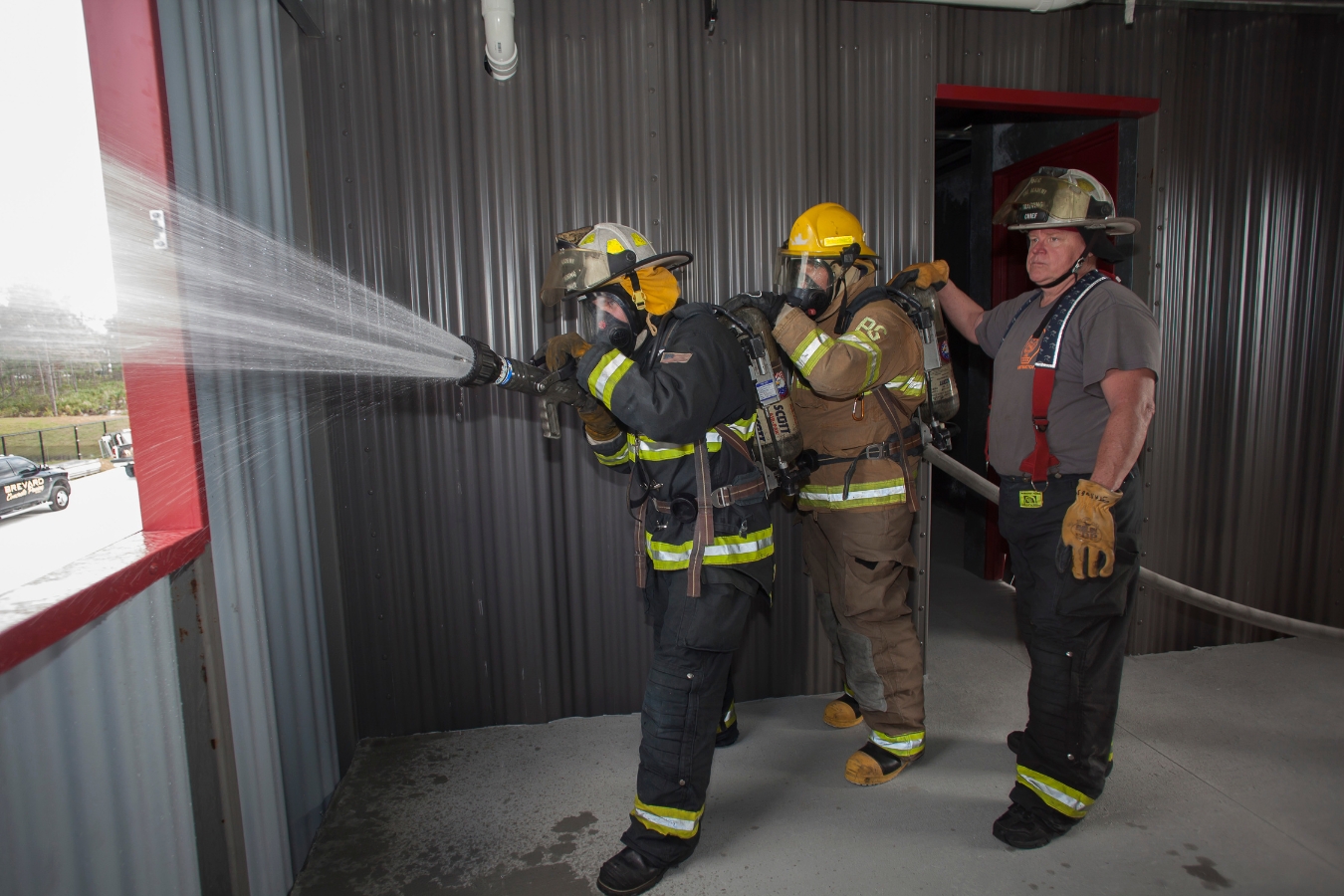 firefighter students working from the inside of the fire academy tower to use a hose and spray water outside of a window to simulate different ways to put out fires