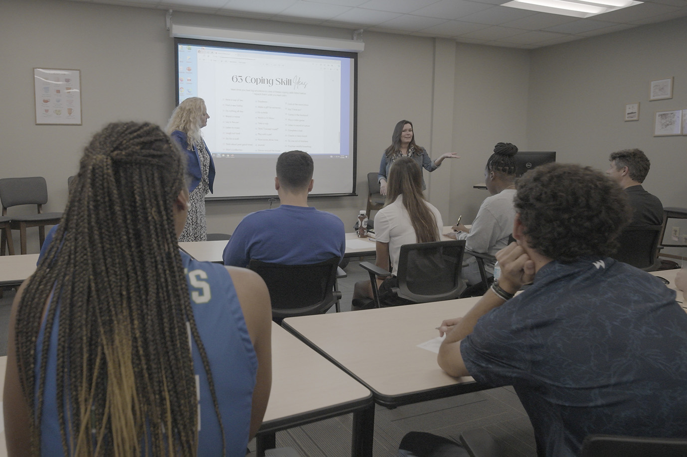 A group of students sitting in a classroom looking at a projector slide.