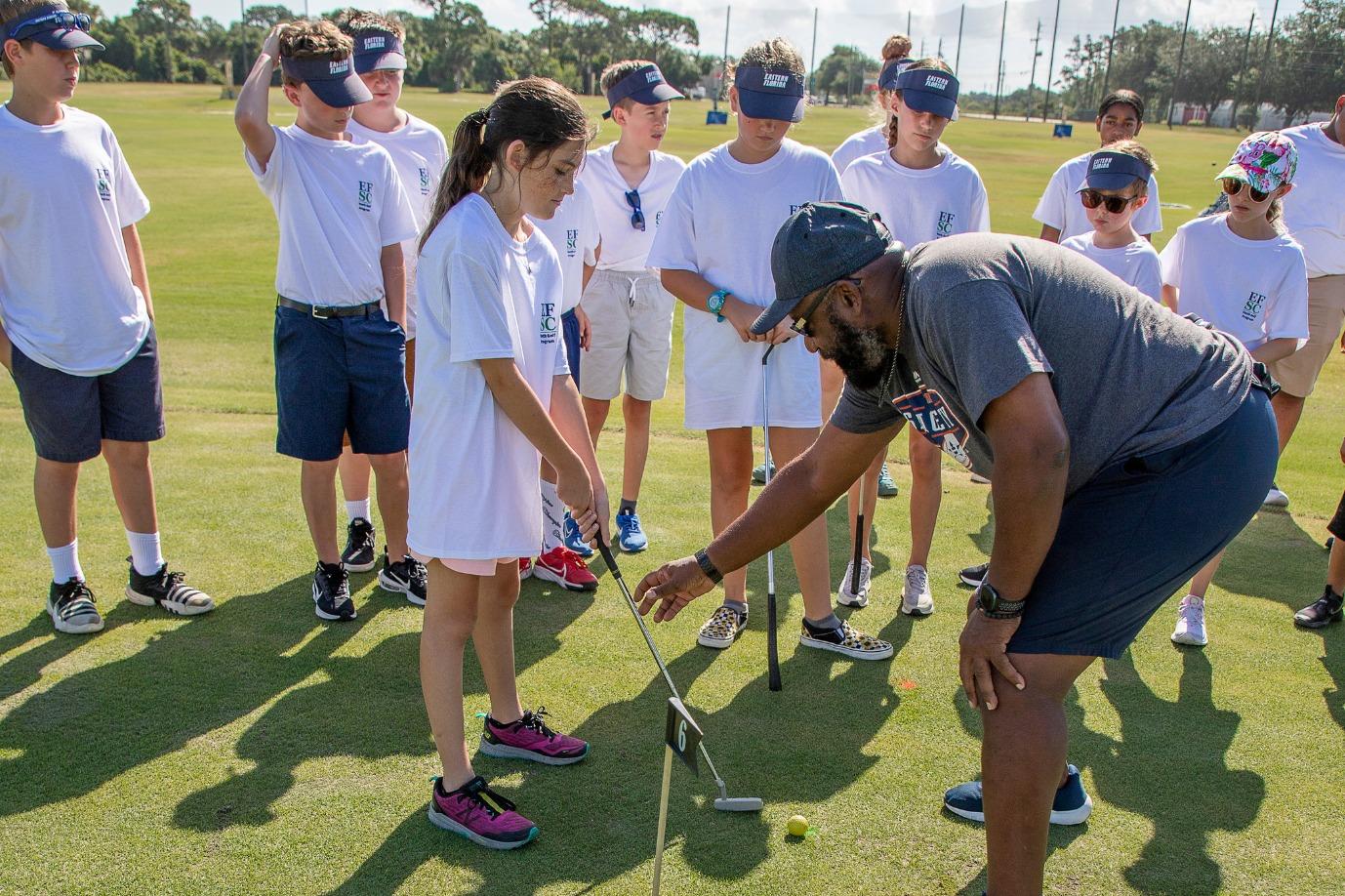 A golf camp coach is helping a young girl learn how to hold and aim a golf club