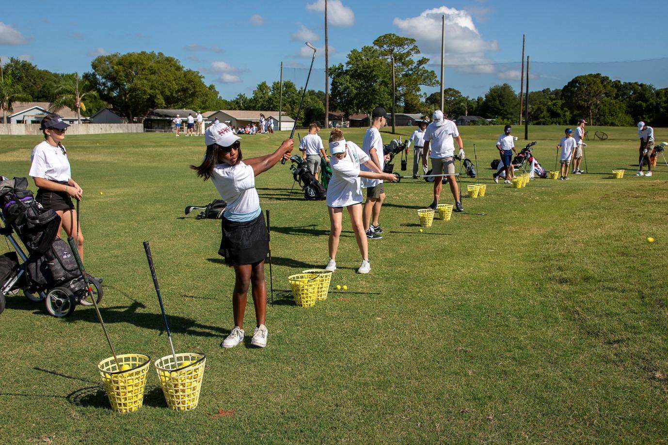 A line of students are swinging their golf clubs on the driving range