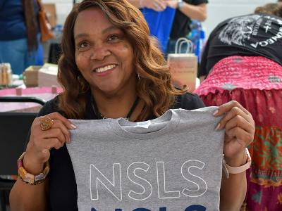 A woman is smiling holding up an NSLS shirt