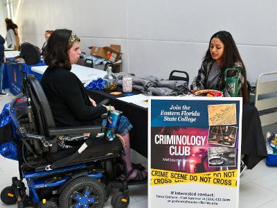Two students are talking at a table with a criminology club sign
