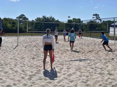 Students playing volleyball on a beach sand course.