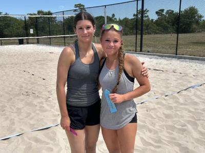 Two students are smiling at the camera on a volleyball court