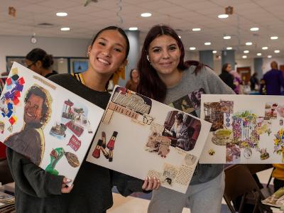 Two students are smiling holding vision boards at an event
