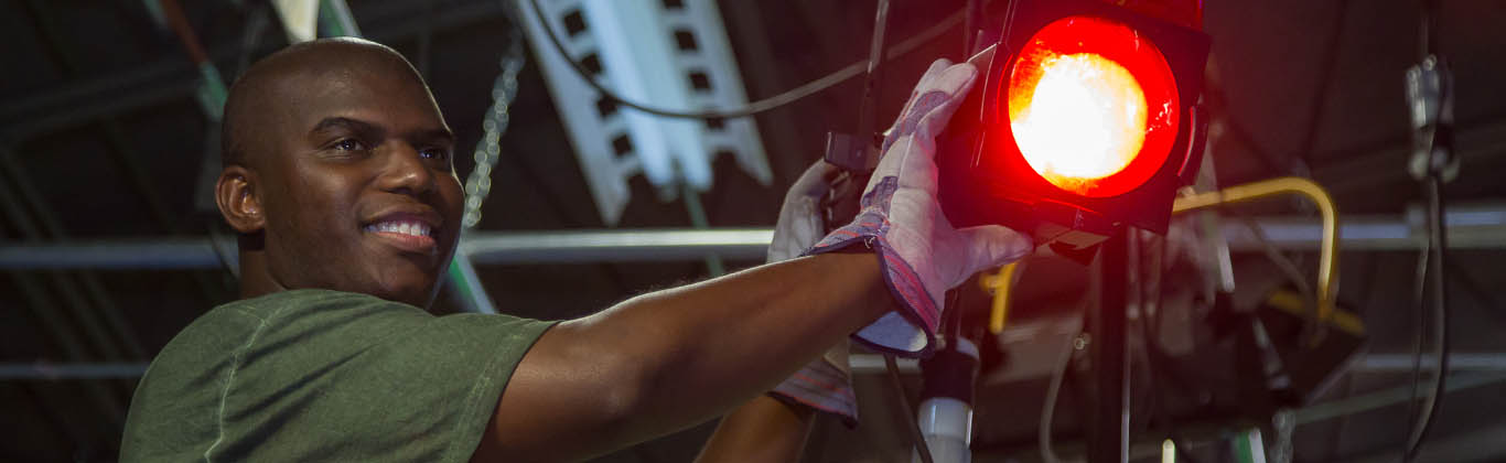 A young, African American man operating a light for a production.