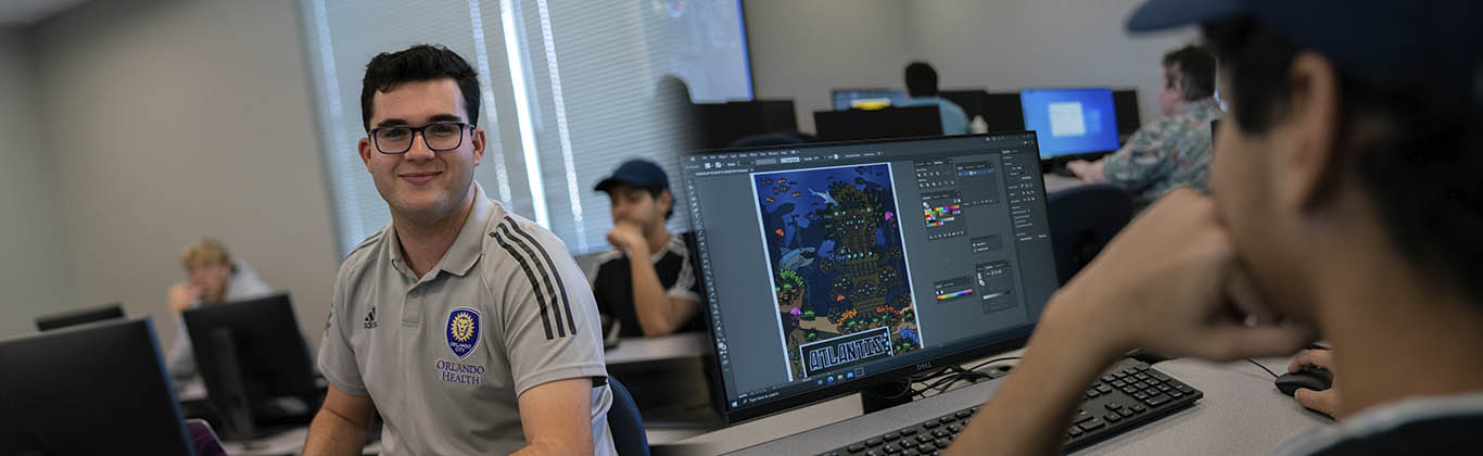 A graphic design student working in Photoshop while another student looks on.