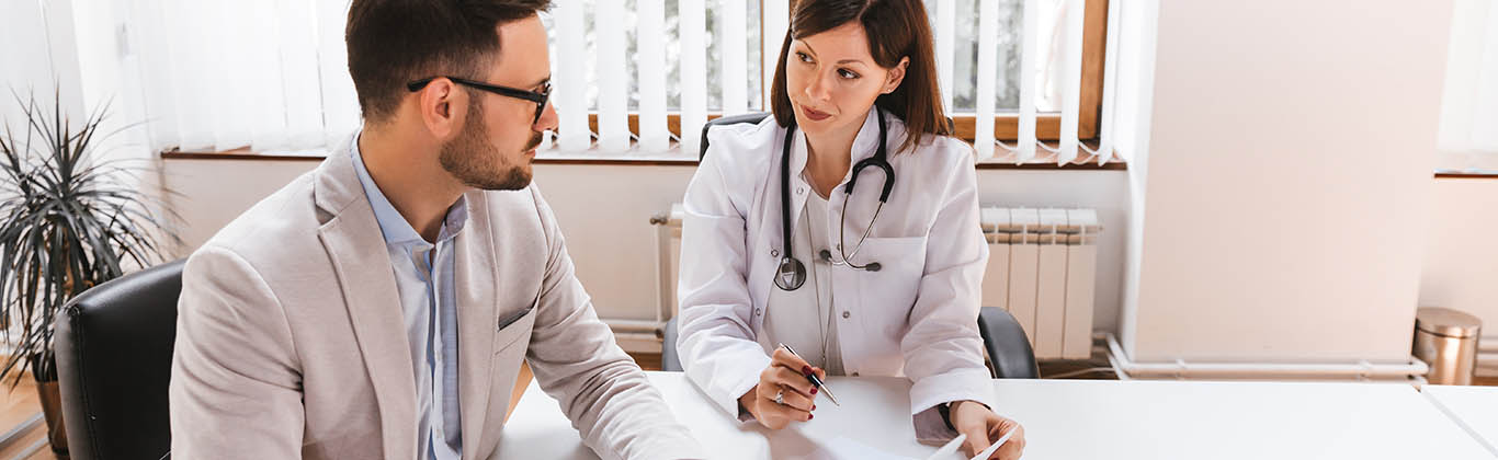 A man with a laptop speaks to a doctor wearing a lab coat and a stethoscope.