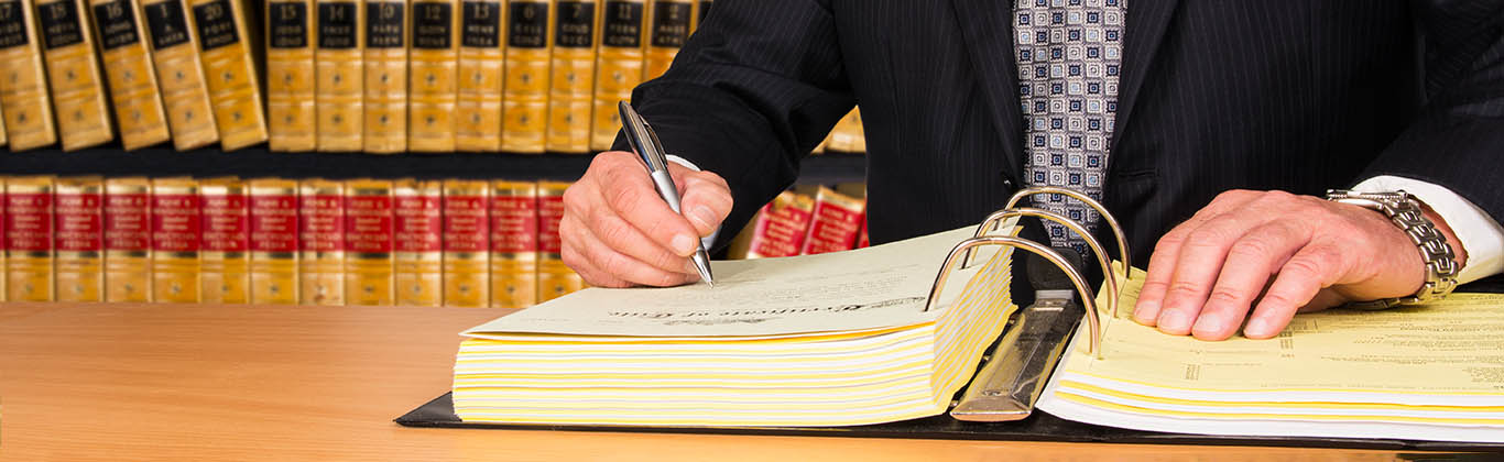 A person in a suit writing in a legal binder with a pen.