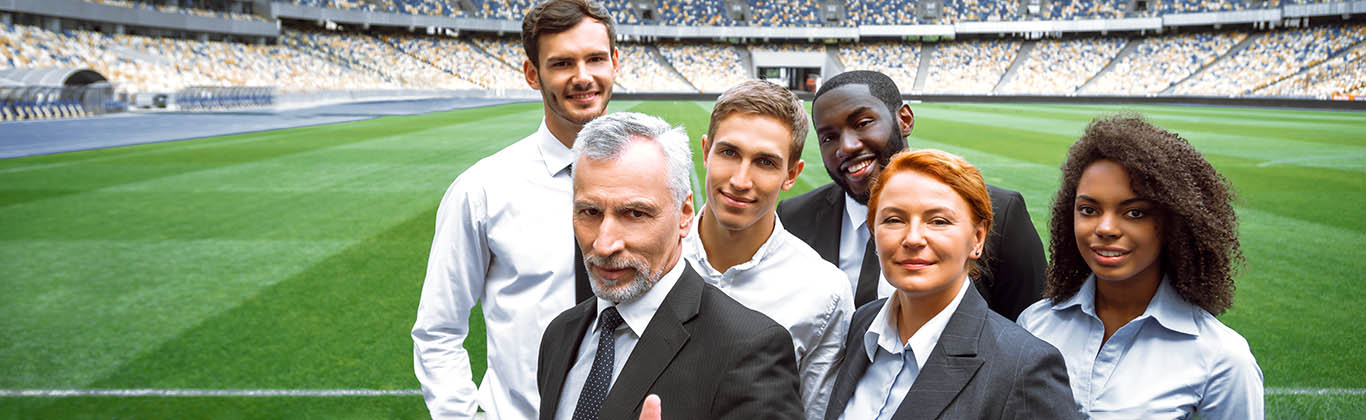 Six professionals in business attire standing in front of a soccer field.