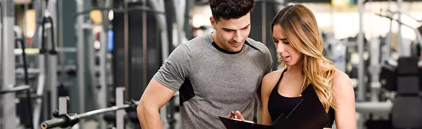 A man and a woman in a gym consulting a clipboard.