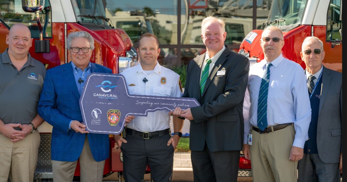EFSC and Canaveral Port Authority members stand in front of two firetrucks while holding a ceremonial key