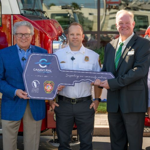 EFSC and Canaveral Port Authority members stand in front of two firetrucks while holding a ceremonial key