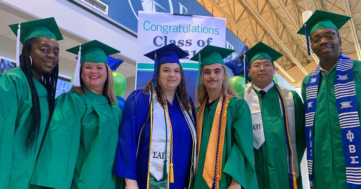 Five graduates in green caps and gowns and one in blue cap and gown