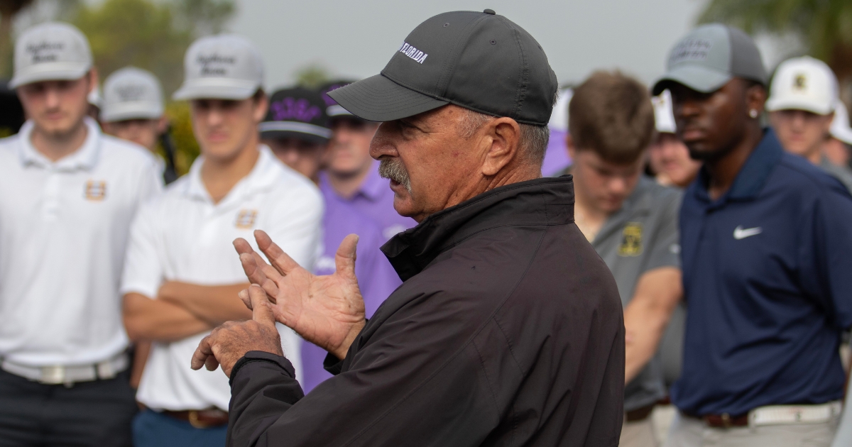 An image of Jamie Howell in a black jacket and dark baseball cap speaks to a group of golfers gathered outdoors, gesturing with both hands while participants in golf attire listen in the background on a golf course.