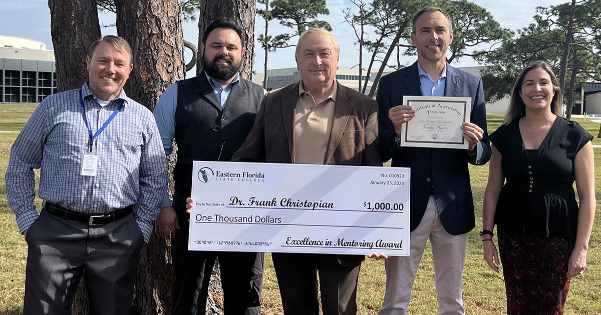 Five people outside with center person, Dr. Frank Christopian, holding a ceremonial $1,000 check