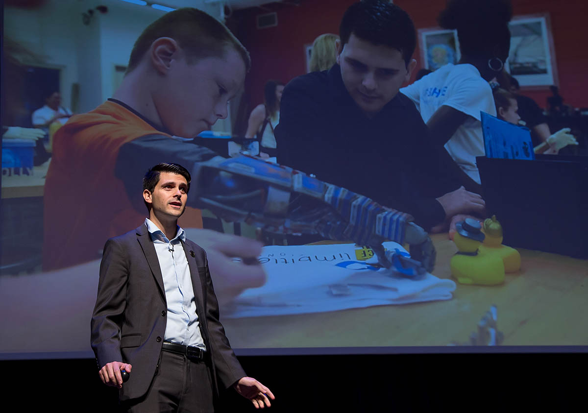 Albert Manero in front of screen with child using prosthetic arm