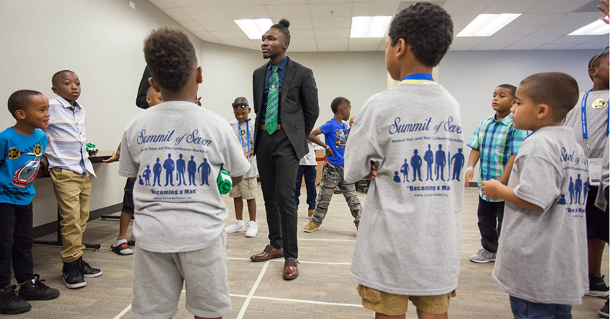 male in suit surrounded by boys in Summit of Seven t-shirts