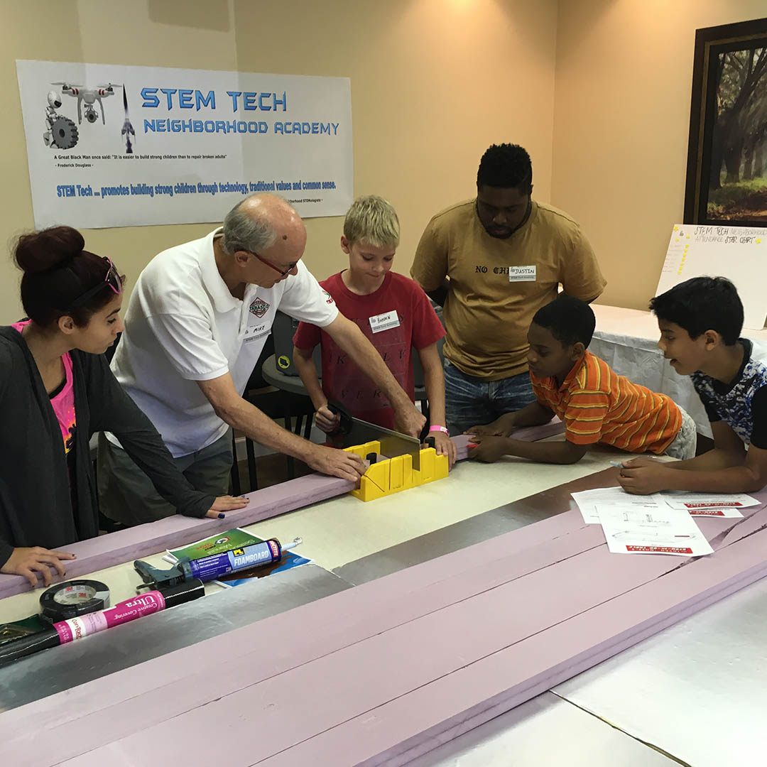 A group of young children gather around an instructor, who demonstrates an interactive measuring activity.